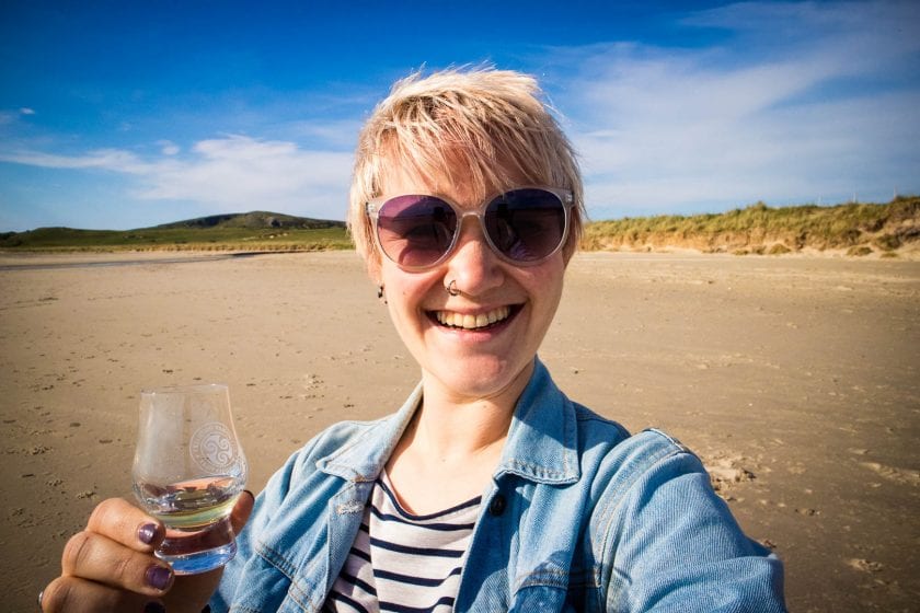 A woman holding a glass of whisky on the beach.