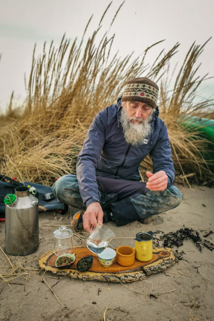 A bearded man performing a tea ceremony on the beach in Ayrshire