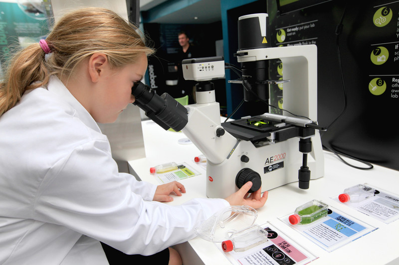 A girl in a white lap coat operating a microscope