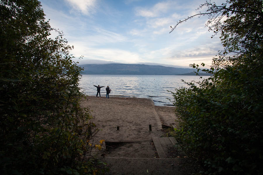 Two people standing by the beach of Loch Lomond.