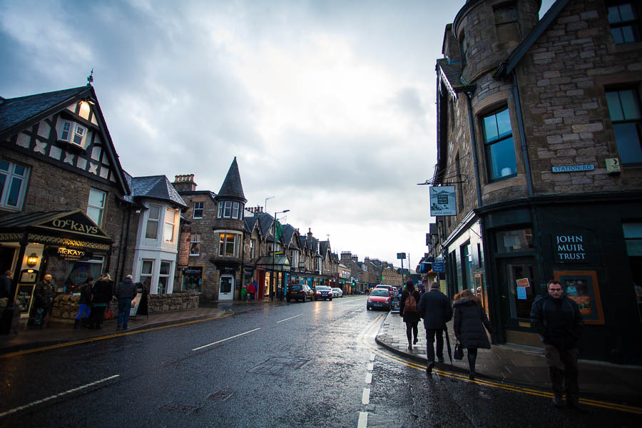 The busy main street of Pitlochry with many shops and pedestrians.