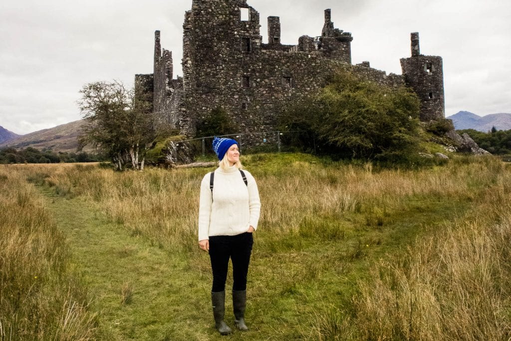 Girl in knitted jumper in front of a castle ruin in Scotland.