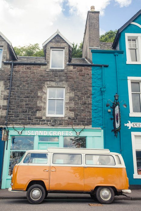 An orange VW bus in front of a colourful shop front in Tobermory.