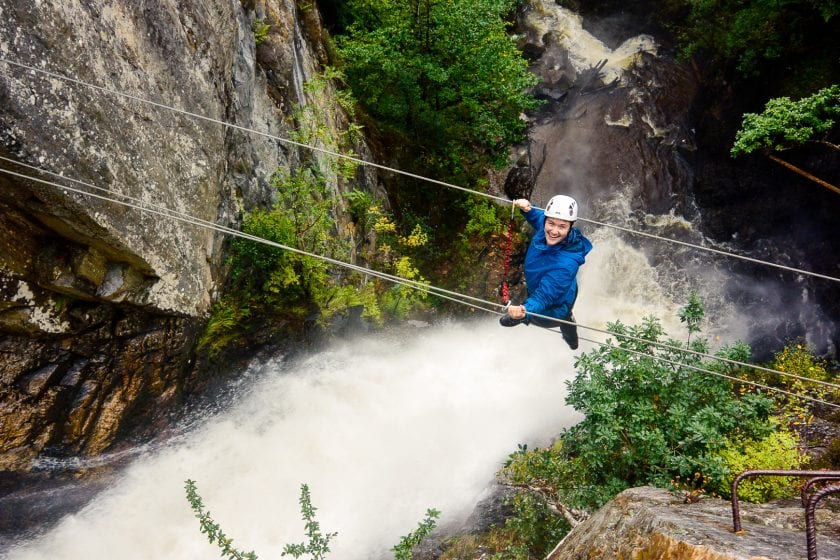 Woman on steel cables above a waterfall climbing the Via Ferrata Scotland in Kinlochleven.