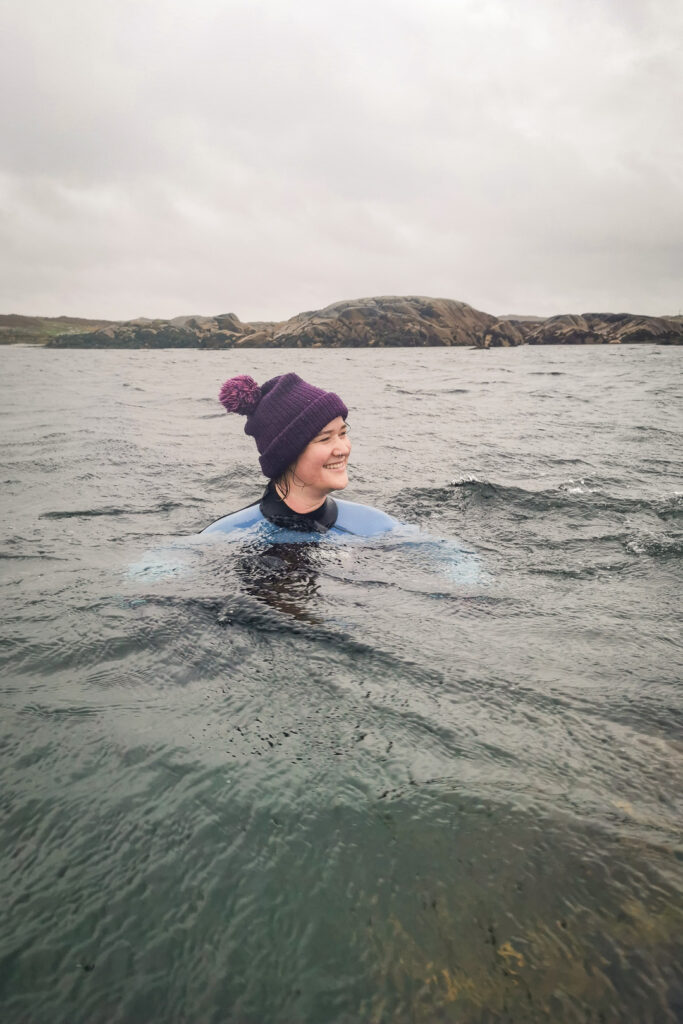 a woman in a wet suit and purple bobble hat wild swimming in the ocean in scotland